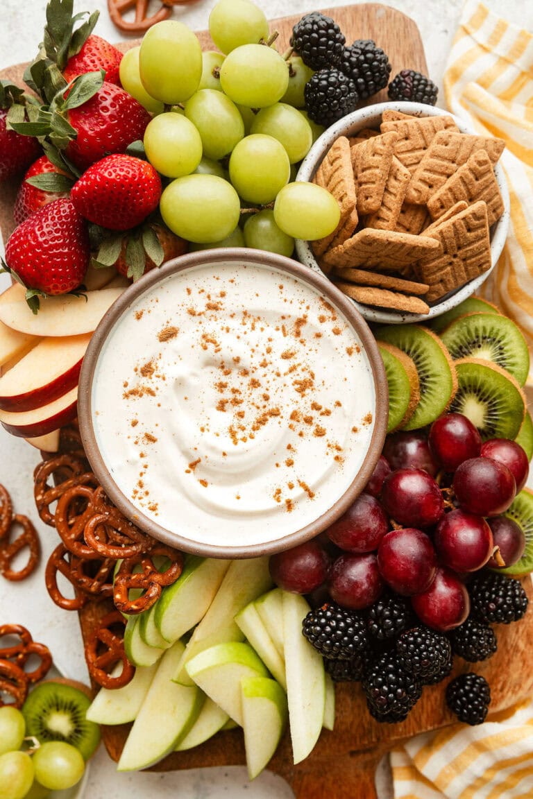 Overhead view of a platter of fresh fruit with a bowl of creamy fruit dip in the middle sprinkled with cinnamon.