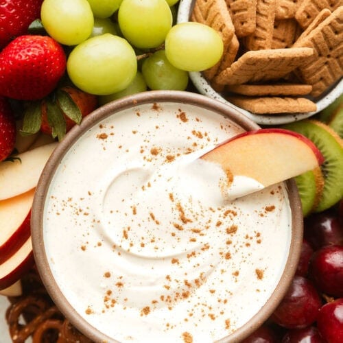 Overhead view of a creamy fruit dip surrounded by fresh fruit and pretzels.