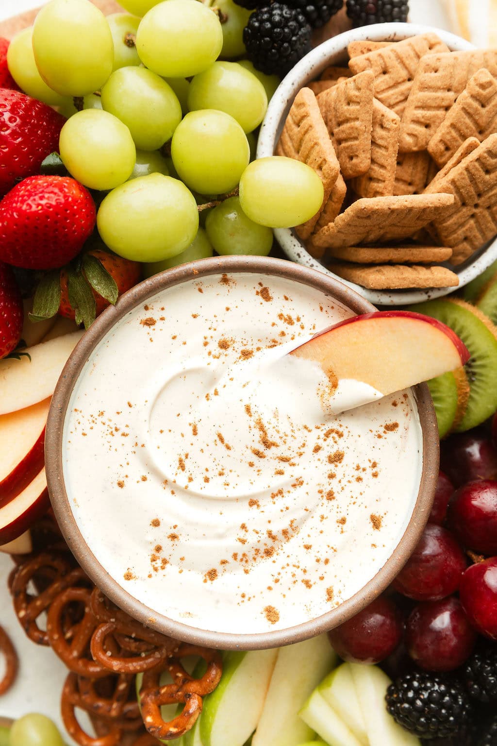 Close up view of a bowl of fruit dip surrounded by fresh colorful fruit and sprinkled with cinnamon.