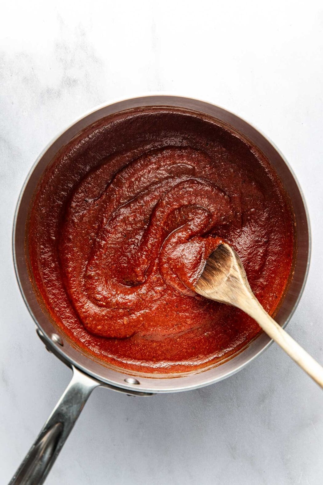 Overhead view of a saucepan filled with Homemade BBQ Sauce being stirred with a wooden spoon