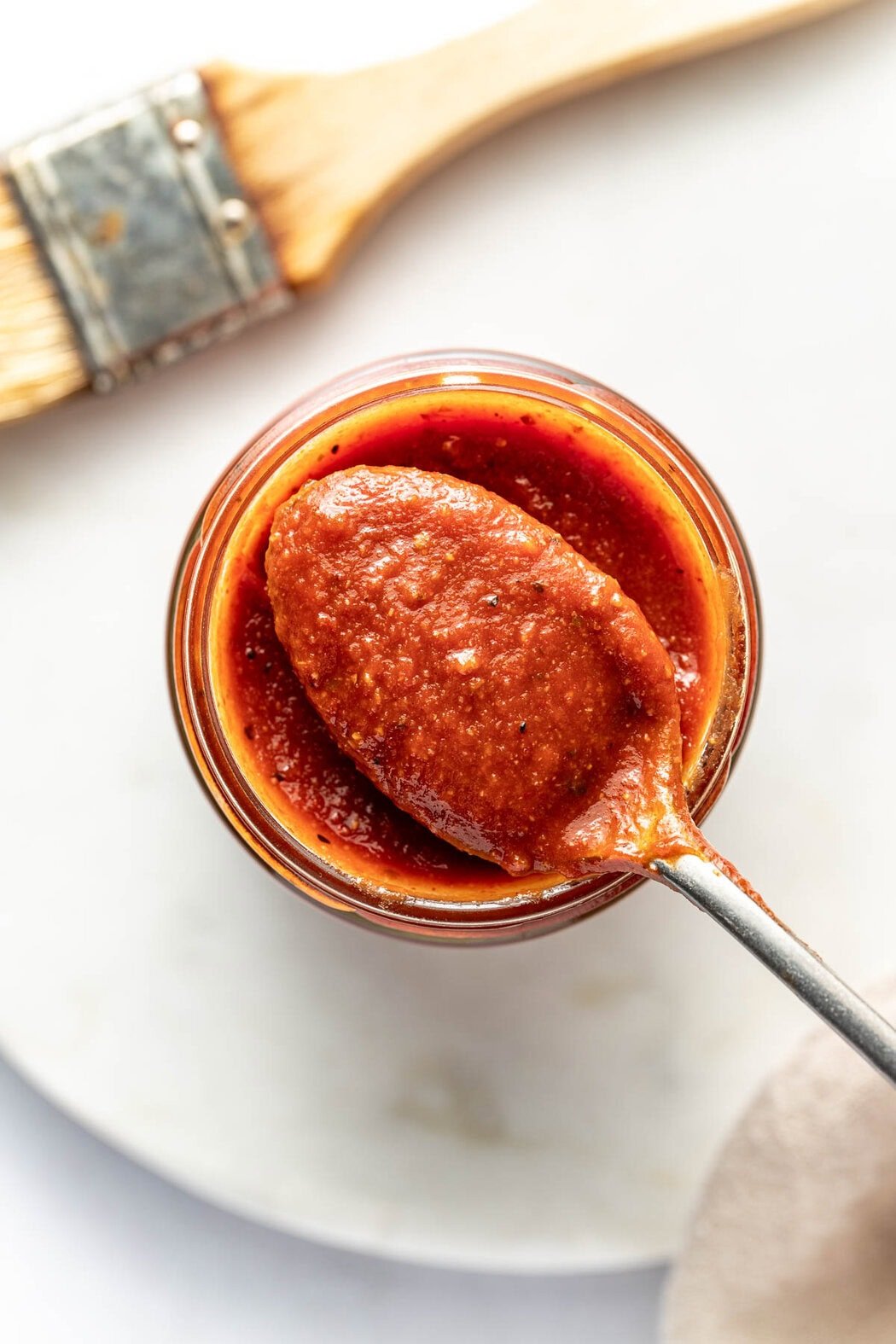 Overhead view of a glass jar of Homemade BBQ Sauce with a spoon bringing out a scoop.