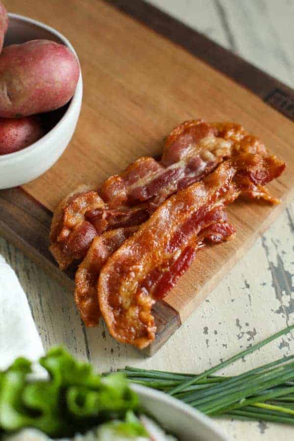 aerial view of bacon, red potatoes, and chives on a cutting board