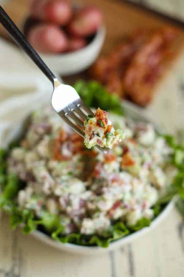 A bite of Bacon Chive Potato Salad on a fork being lifted towards the camera
