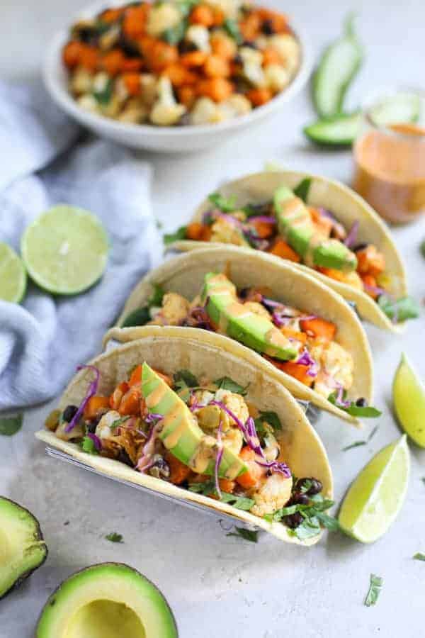 3 Tacos in a rack with avocado slices on top of each. 