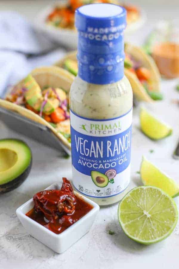 Bottle of Primal Kitchen Ranch Dressing with some chipotle peppers in a pinch bowl and slices of lime. 