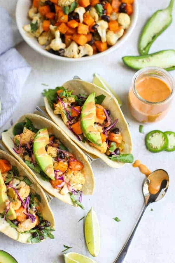 Overhead view of Vegan Cauliflower Sweet Potato Tacos with sauce. Spoon with sauce dripping from it lying next to the tacos. 