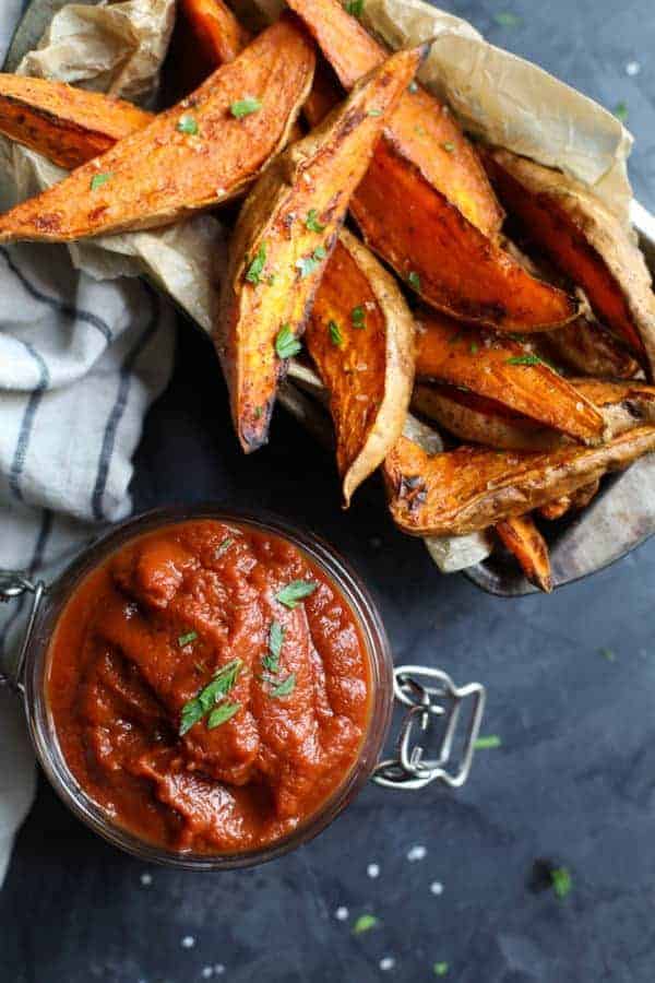 Close up shot of BBQ sauce with roasted sweet potato wedges on a black table top. 