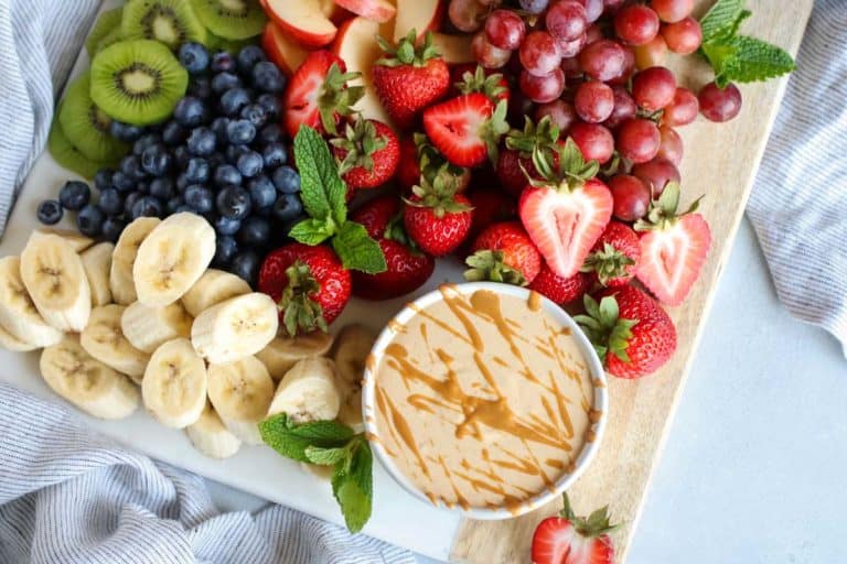 Overhead view of peanut butter fruit dip in small white bowl on tray with fresh fruit