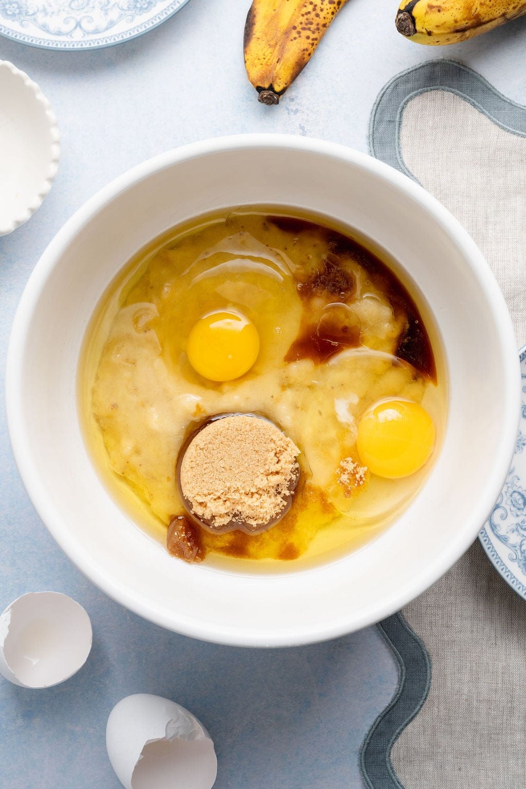 Overhead view of a white bowl filled with wet ingredients for Banana Blueberry Muffins including 2 eggs ready for stirring. 