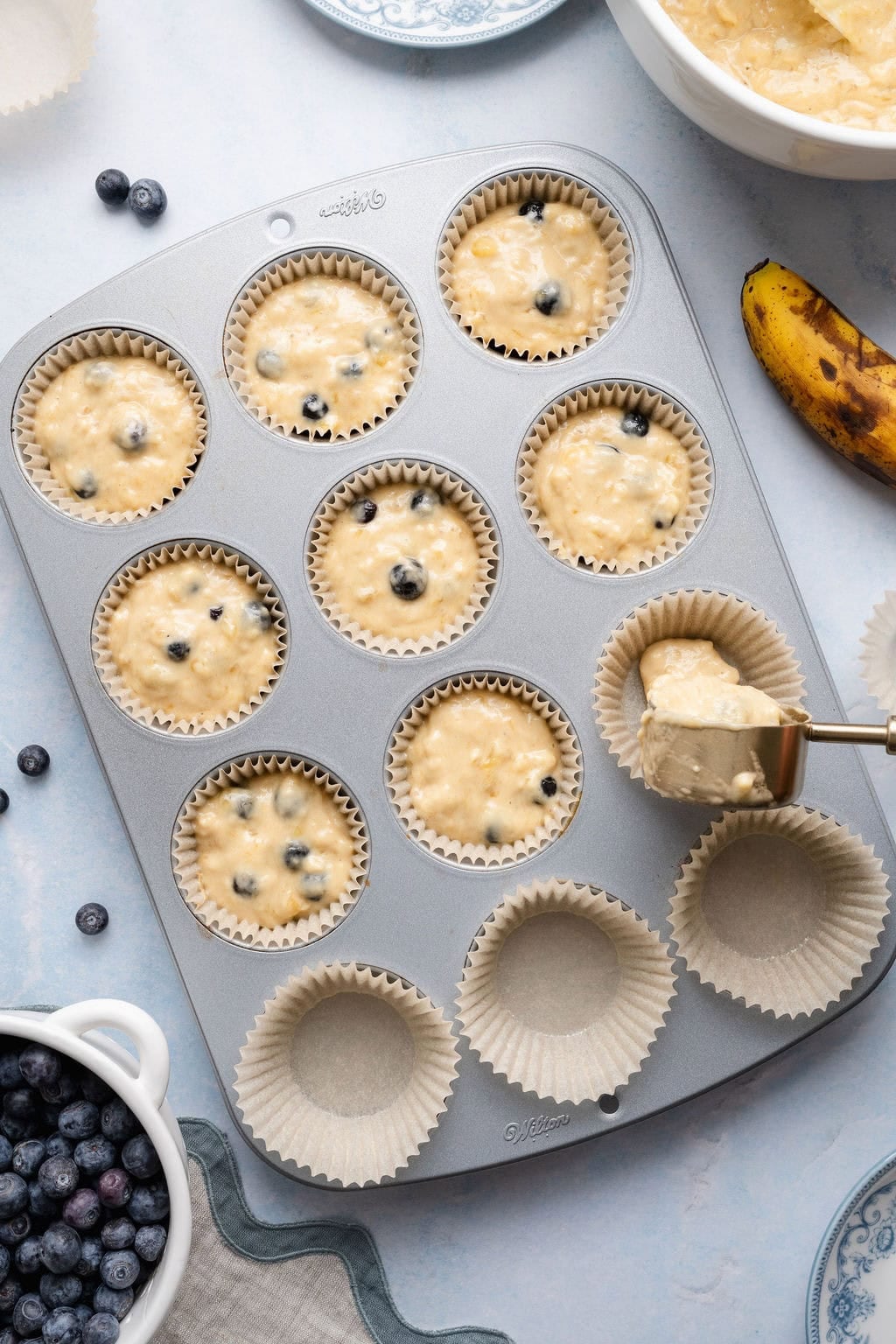 Overhead view of a muffin pan filled with liners and dough being poured into each well. 