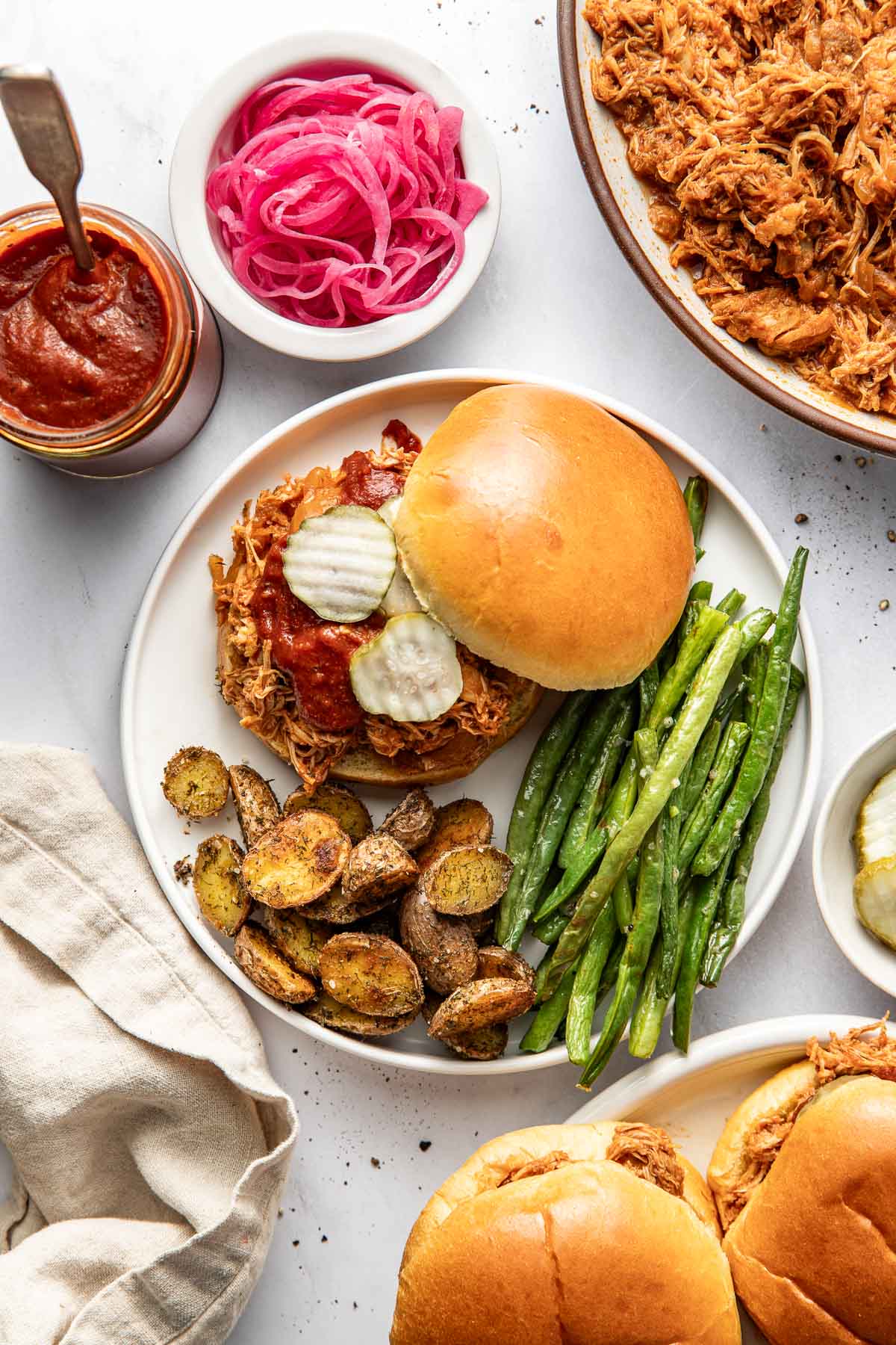 Overhead view of a plate filled with a BBQ Pulled Chicken sandwich, green beans, and roasted potatoes.