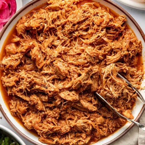 Overhead view of a bowl of BBQ Pulled Chicken with a tong on the side of the bowl.