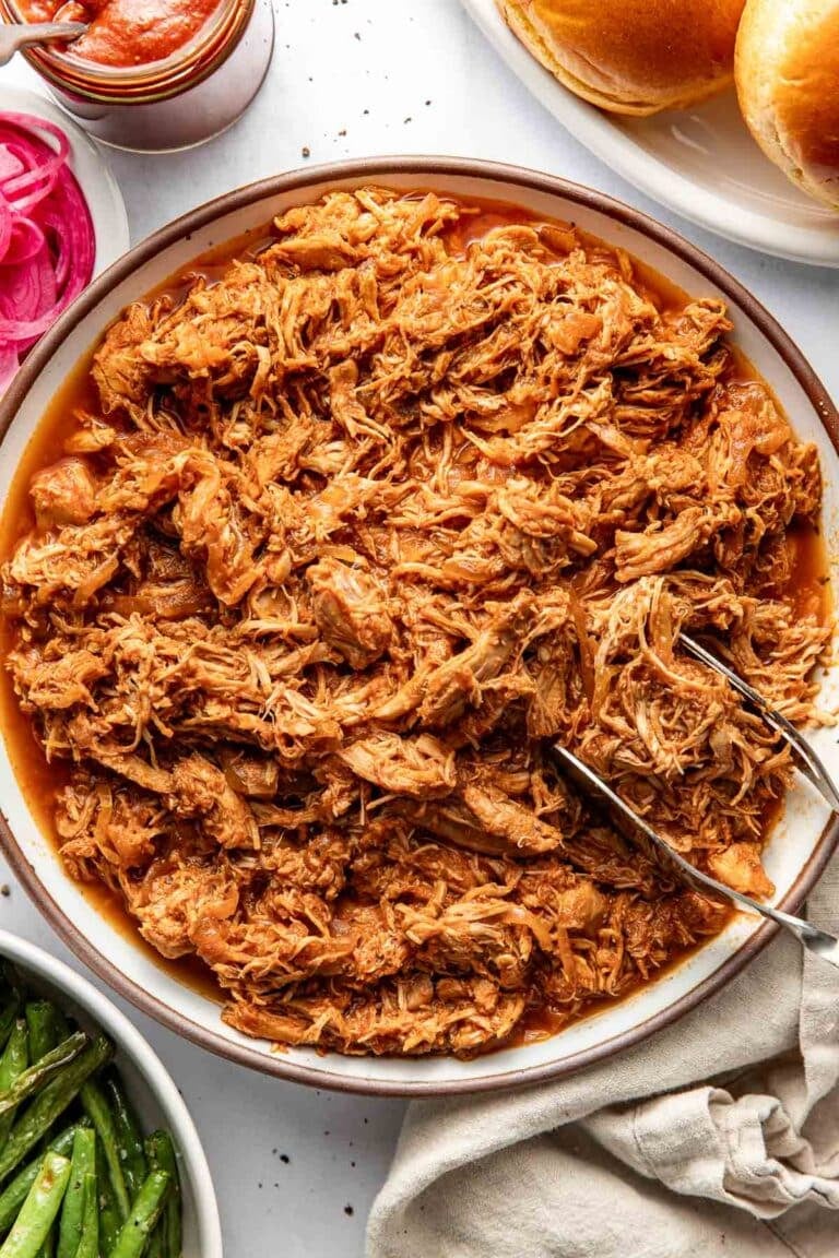 Overhead view of a bowl of BBQ Pulled Chicken with a tong on the side of the bowl.