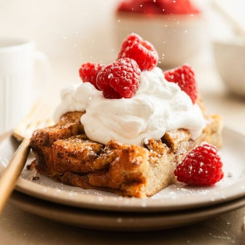 Close up view of a piece of French Toast Casserole topped with whipped topping, fresh raspberries, and sprinkled with powdered sugar.