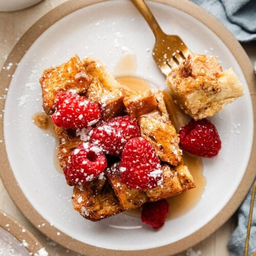 Overhead view of a plate of filled with a piece of French toast casserole topped with raspberries and sprinkled with powdered sugar.