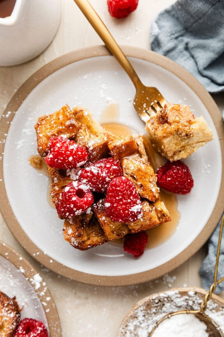 Overhead view of a plate of filled with a piece of French toast casserole topped with raspberries and sprinkled with powdered sugar.