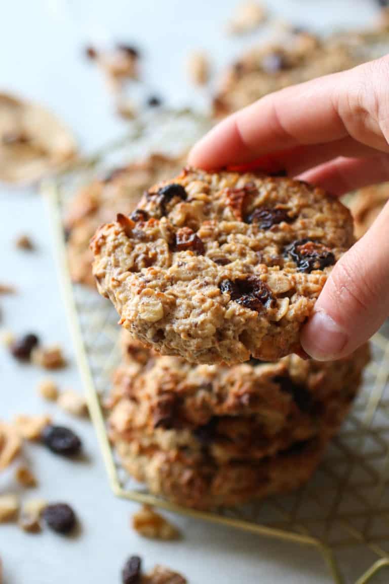 A hand grabbing an Apple Cinnamon Breakfast Oat Cookie off a cooling rack. 