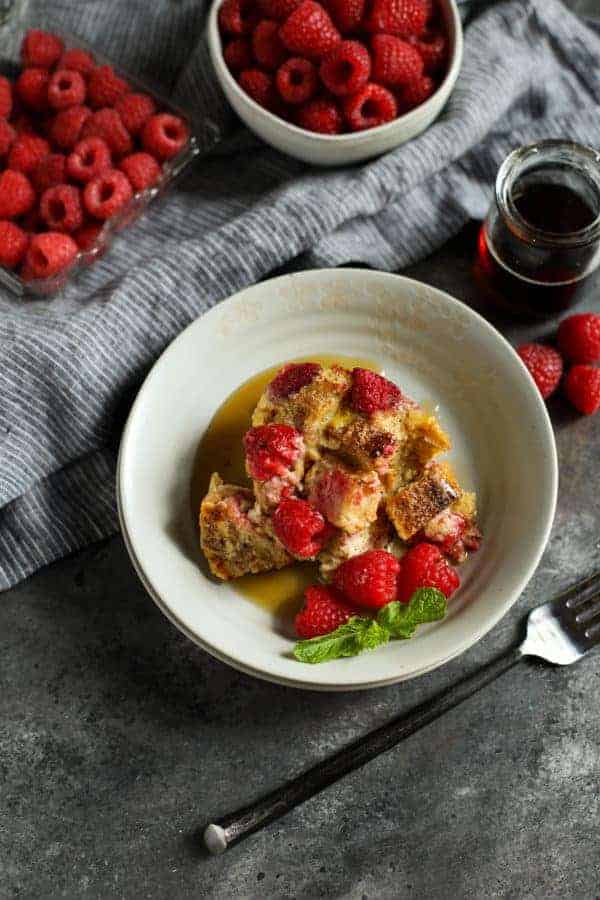Overhead view of a serving of Instant Pot Raspberry French Toast Casserole drizzled with maple syrup and surrounded by fresh raspberries. 