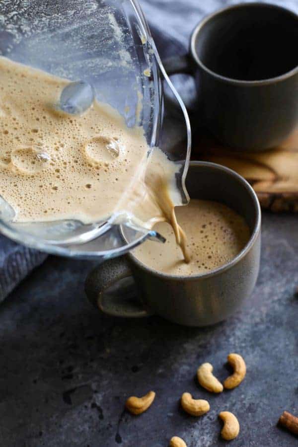 Pouring Snickerdoodle Cashew Coffee from a blender container into a grey mug. 