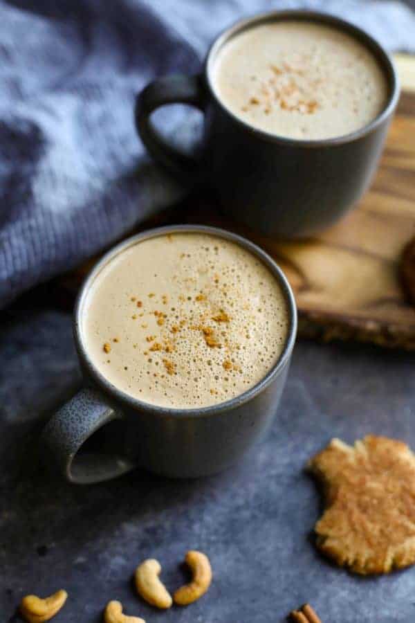 Two grey mugs of cream Snickerdoodle Cashew Coffee - with a cookie on the side. 