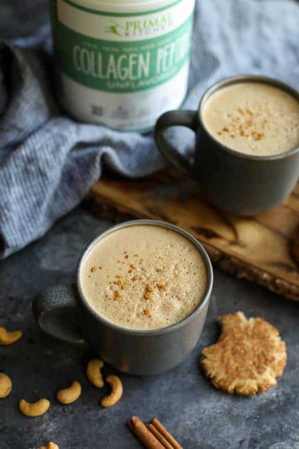 Looking down on two mugs of Snickerdoodle Cashew Coffee next to a cookie with a bite out of it and a canister of Primal Kitchen Collagen Peptides. 