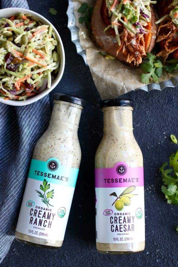 aerial view of bottles of Tessemae's Organic Creamy Ranch and Creamy Caesar dressings and a bowl of slaw and sweet potato stuffed with pulled BBQ chicken