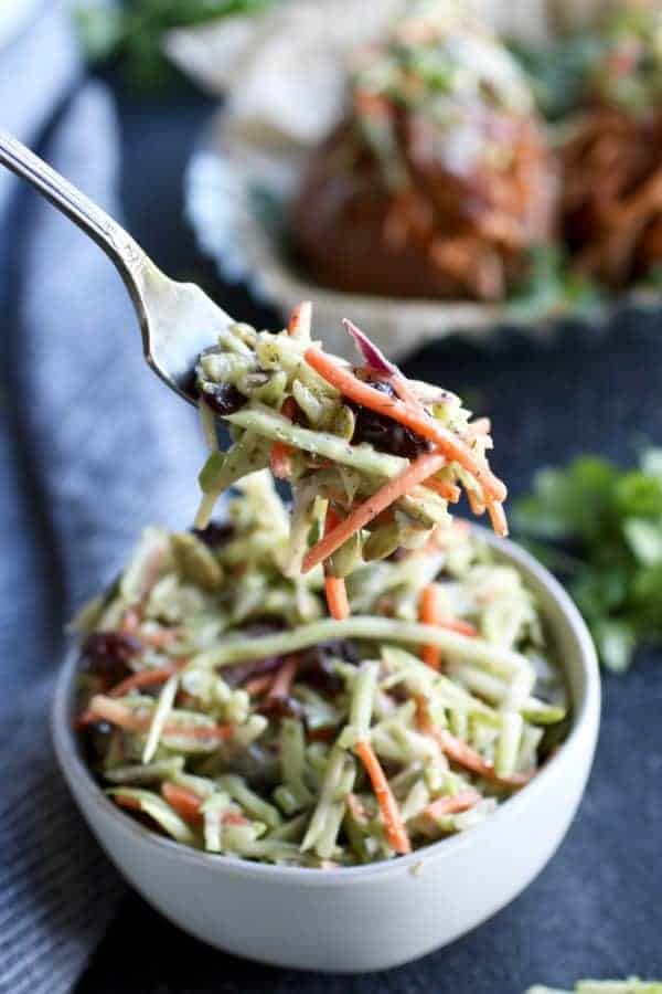 Simple Slaw on a fork lifted from a white bowl full of slaw