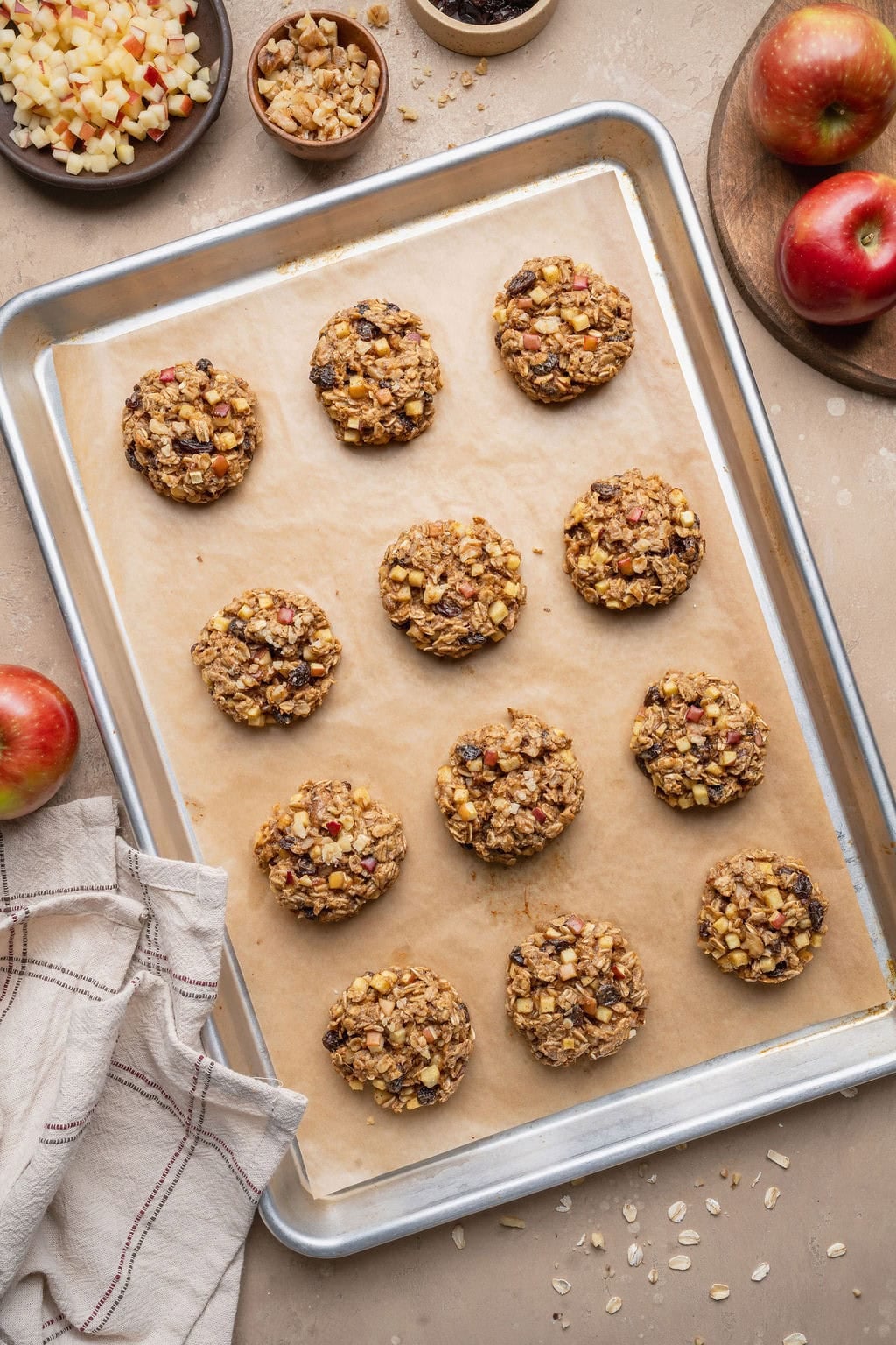 A parchment paper-lined baking sheet with twelve baked apple oatmeal cookies.