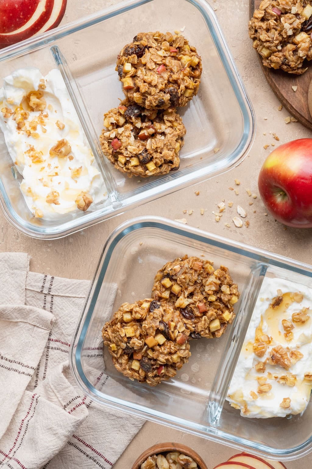 Two glass containers with yogurt topped with honey and walnuts and two apple oatmeal cookies.