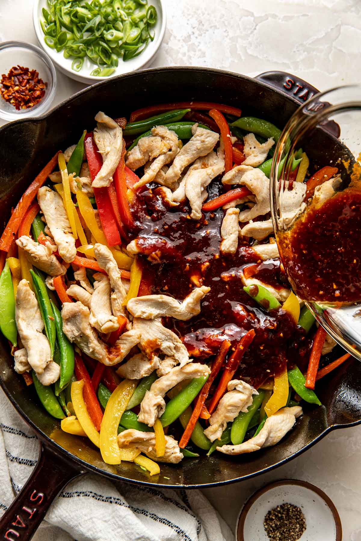 Overhead view of a skillet of Chicken Stir Fry with a deep brown colored sauce being poured over the top.