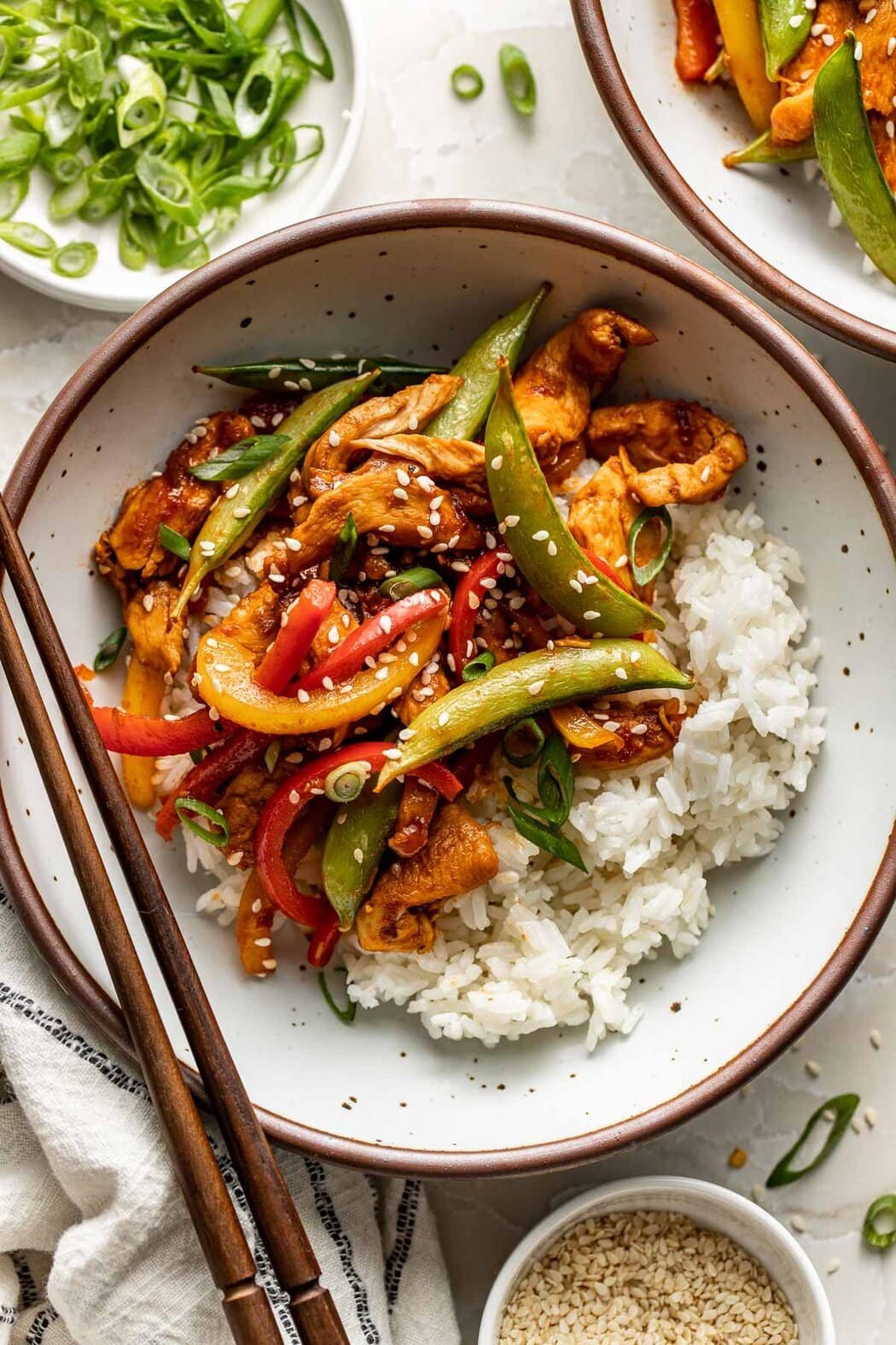 Overhead view of a plate of Chicken Stir Fry on top of a bed of rice topped sesame seeds and green onions.