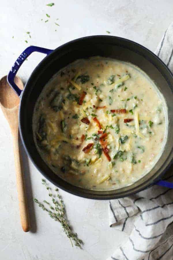 Overhead view of Loaded Cheesy Cauliflower Soup in a pot with a wooden spoon 