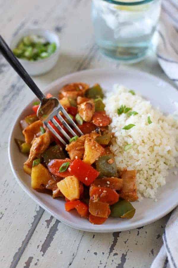 Close up view of Sweet and Sour Chicken with a side of rice on a white plate with a fork 