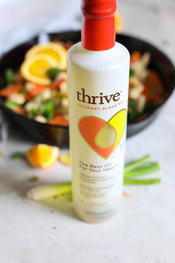 Thrive Culinary Algae Oil in front of a pan of ingredients for Orange-Ginger chicken Stir Fry