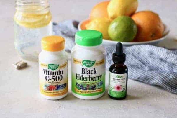 Nature's Valley Vitamin C-500, Black Elderberry, and Echinacea bottles in front of lemon water and citrus fruits in a bowl