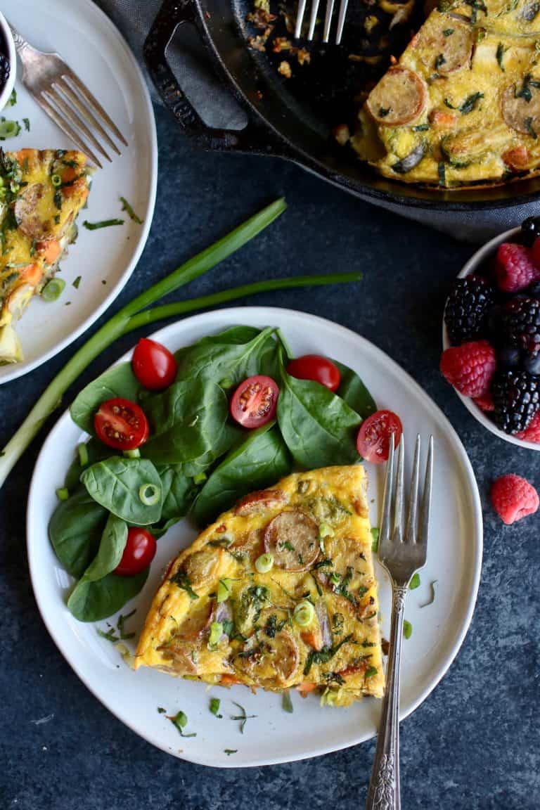 Overhead view of a plate with a piece of Sweet Potato Chicken Sausage Egg Bake next to greens and sliced cherry tomatoes. 