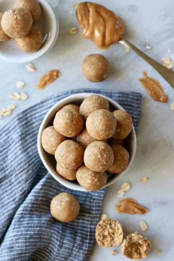 Overhead view of 3-Ingredient Peanut Butter Bites in a white bowl with a spoonful of peanut butter on the side