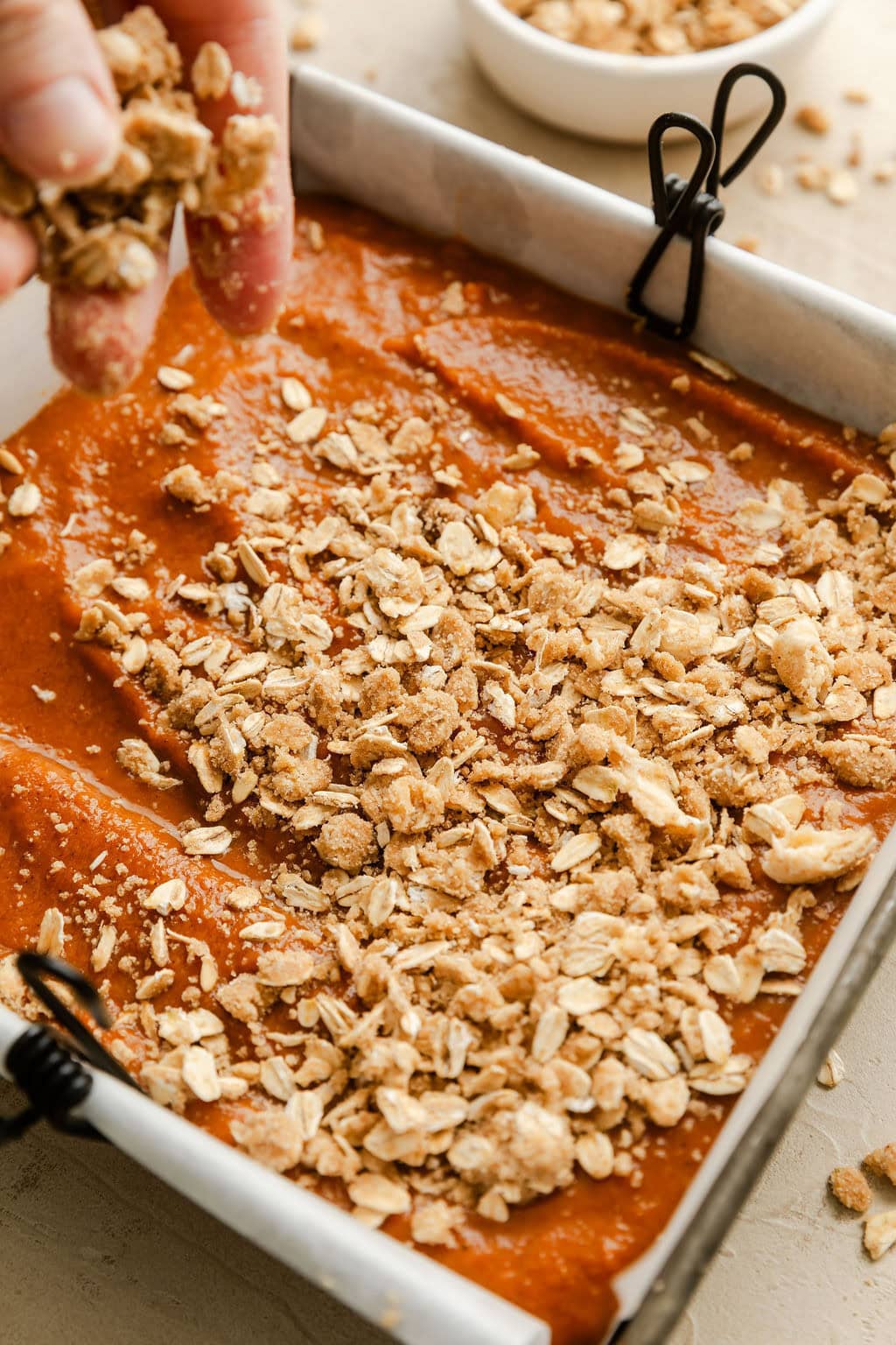Close up view of a baking dish filled with a pumpkin mixture being topped with an oat crumble. 