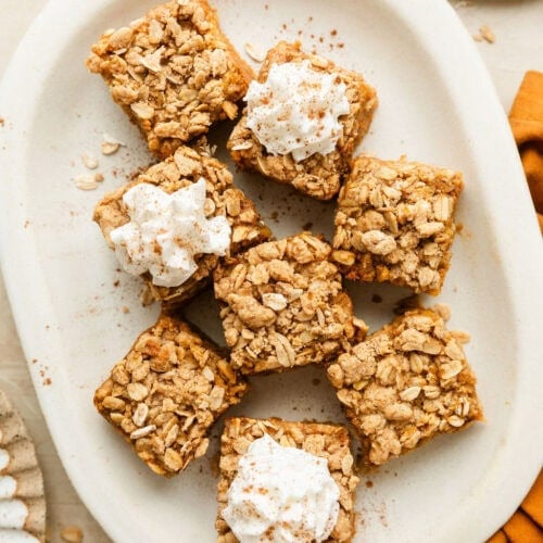 Pumpkin pie bars on white platter, cut into small squares, some with whipped topping.