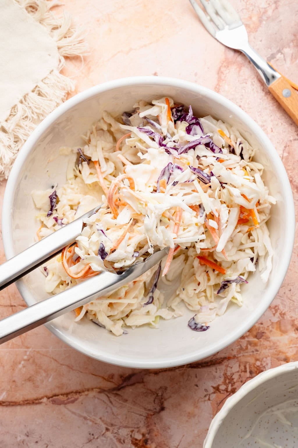 Overhead view of a white bowl filled with creamy coleslaw.