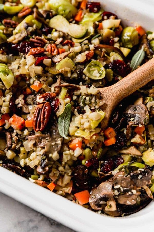 A wooden spoon scooping up healthy cauliflower stuffing with pecans and rosemary sprigs 