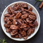 A speckled white plate full of holiday spiced nuts and topped with sea salt flakes
