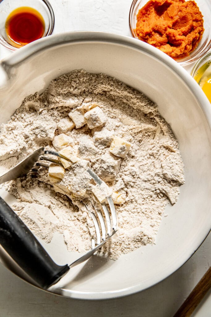 Overhead view of a bowl of dry ingredients for Gluten-Free Pumpkin Spice Scones being mixed with a pastry cutter. 