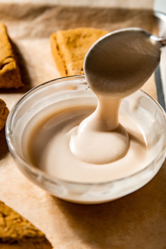 Close up view of a spoon mixing icing for Gluten-Free Pumpkin Spice Scones. 