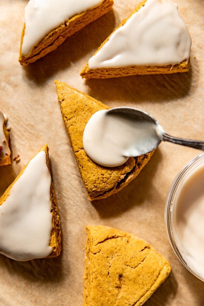 A spoon spreading icing on top of Gluten-Free Pumpkin Spice Scones. 