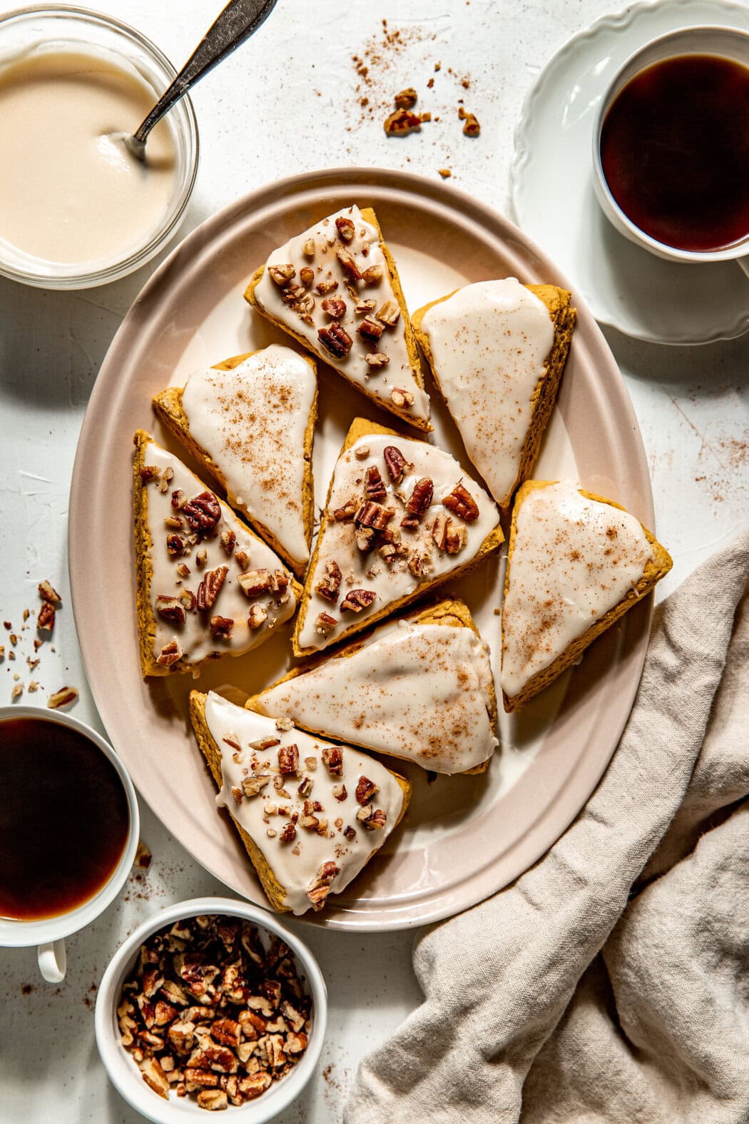 Overhead view of a plate of Gluten-Free Pumpkin Spice Scones topped with icing and pecan pieces. 