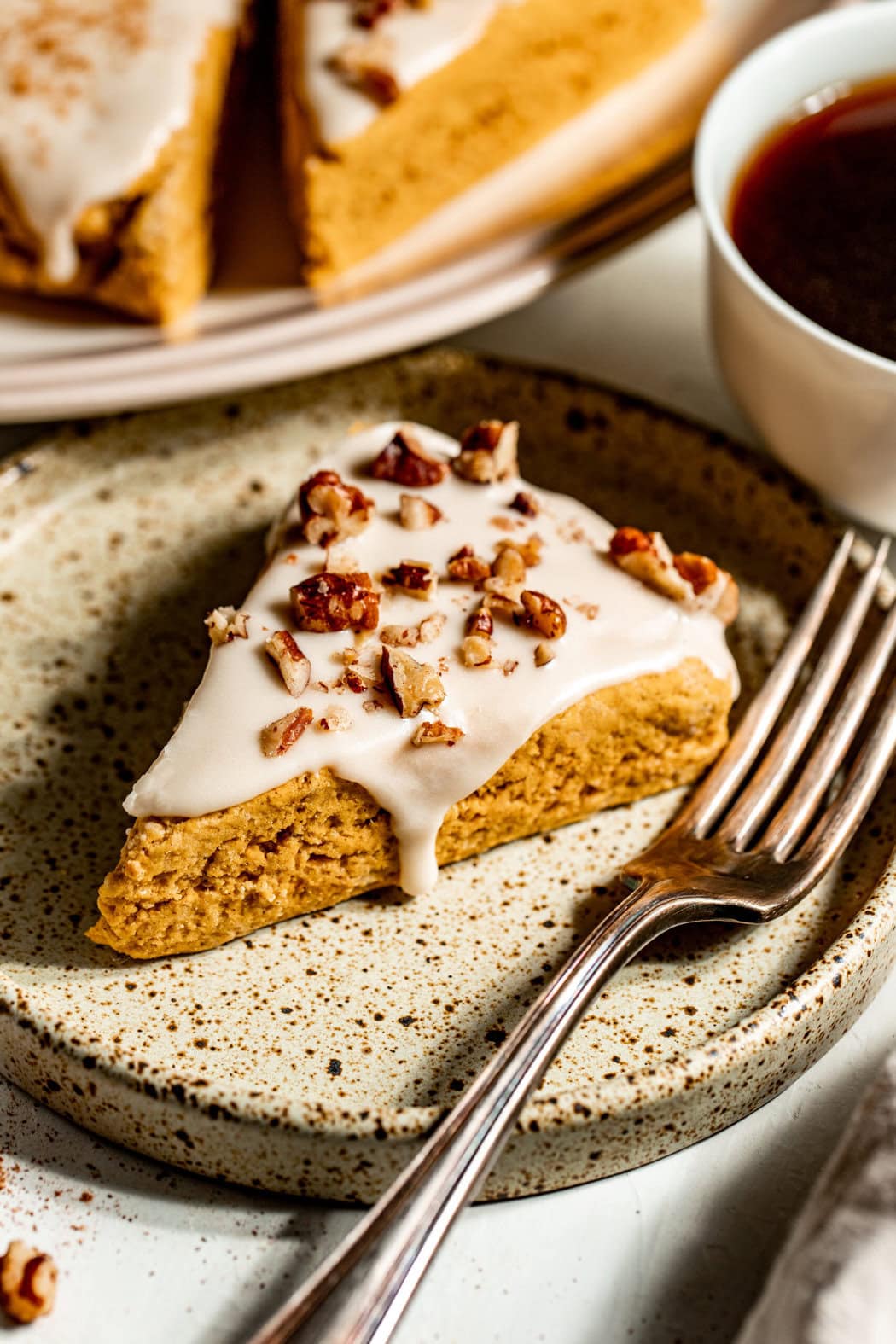 Close up view of a piece of Gluten-Free Pumpkin Spice Scone topped with icing and pecan pieces. 