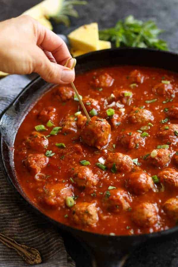 Meatball being picked out of a skillet with a person holding a toothpick