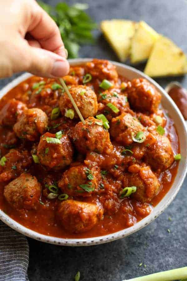 Close up view of a person picking a meatball out of a bowl with a toothpick 