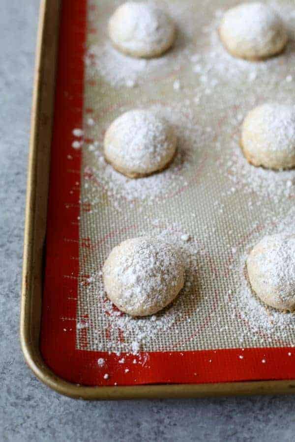 Close view of baked teacakes covered in powered sugar on a cookie sheet